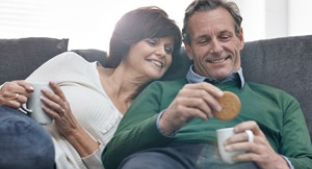 Smiling middle age couple on sofa dunking McVitie's digestive biscuits in tea cup