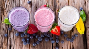 smoothies purple, pink and white smoothie on wooden table surrounded by berries